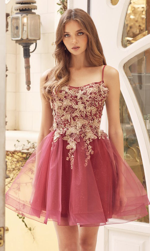 A woman stands indoors wearing the Short A-Line Butterfly Homecoming Dress 902, a burgundy babydoll party dress featuring intricate gold embroidery and a tulle skirt.